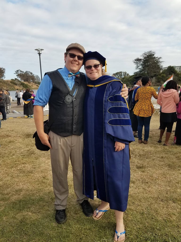 Dr. Laura Hooton, right, in Ph.D. graduation robes with husband at outdoor graduation, Santa Barbara