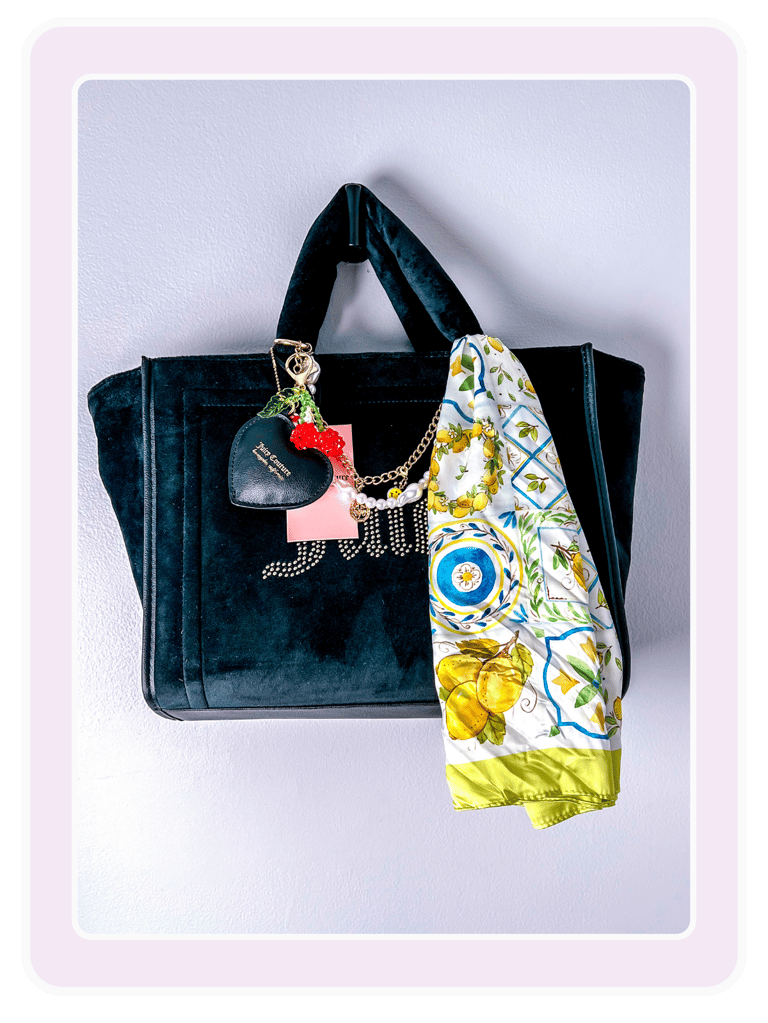 Black velvet Juicy Couture tote bag with heart charms and a lemon print silk scarf hanging on a wall.