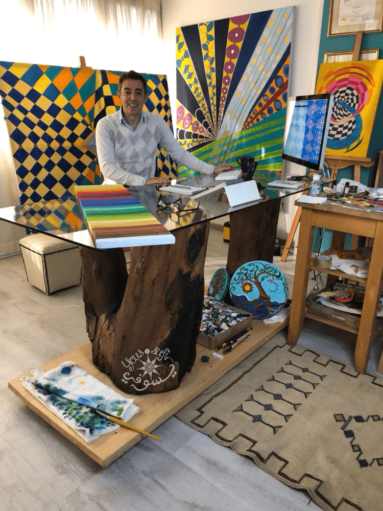 Artist Yous sitting with many oil paintings around