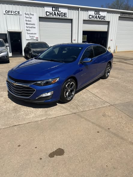 Blue Chevrolet Malibu sedan parked in front of an automotive repair shop and oil change service center.