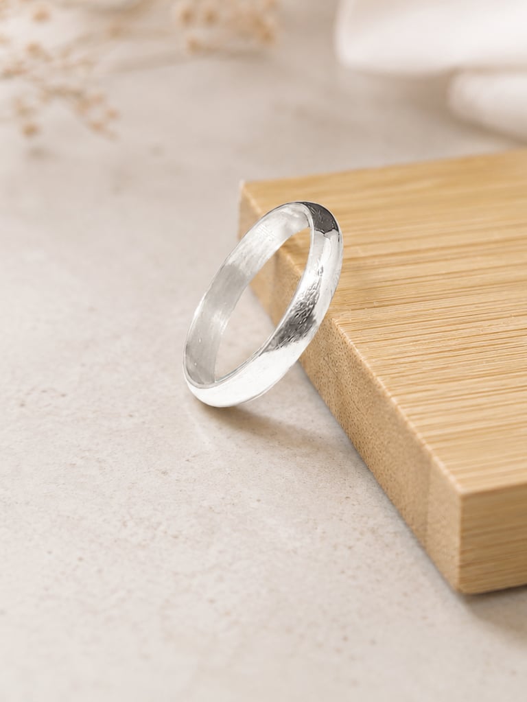 Polished 999 fine silver wedding band resting on a bamboo wood block with a minimalist aesthetic.