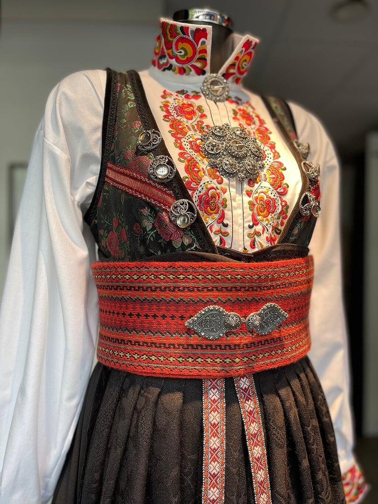 Black Bunad with a wide red belt and embroidered white shirt on a mannequin