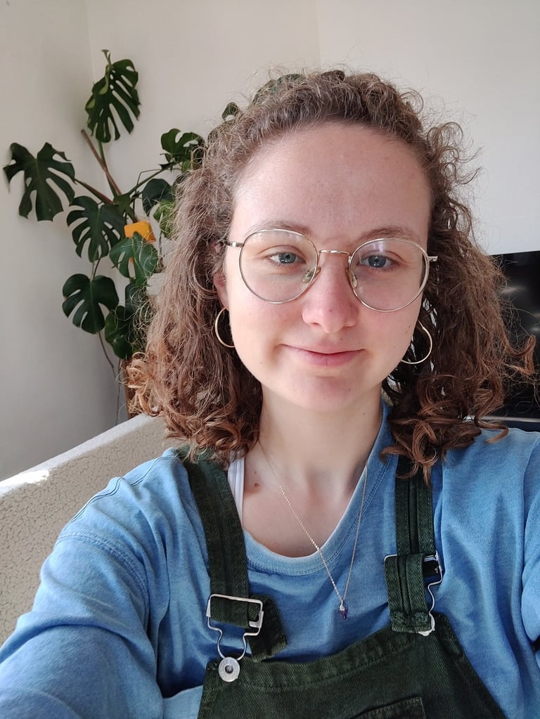 a selfie of Eleanor who is a curly haired queer women in her late twenties wtih glasses and dungarees