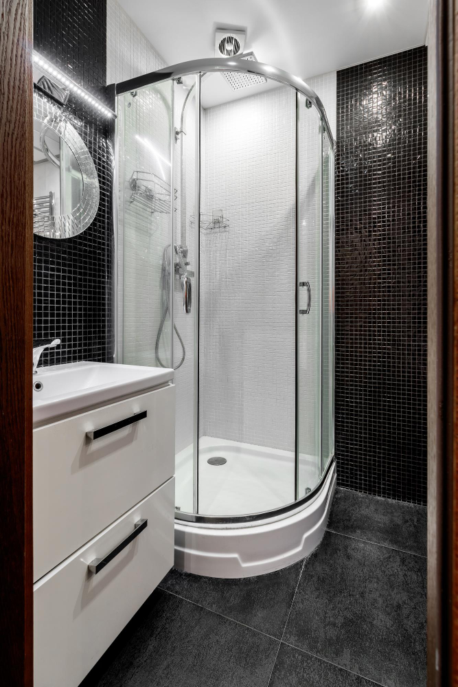 Bathroom with corner glass shower enclosure and black mosaic tiled walls