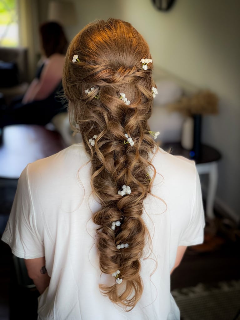 Brunette bride with long boho braid adorned with delicate white flowers, styled in loose romantic curls for wedding day hair.