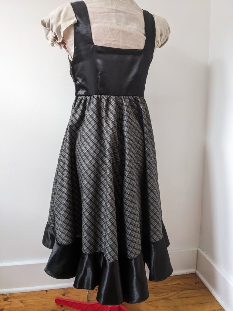 The back of a black/gold plaid and black satin flowy cocktail dress