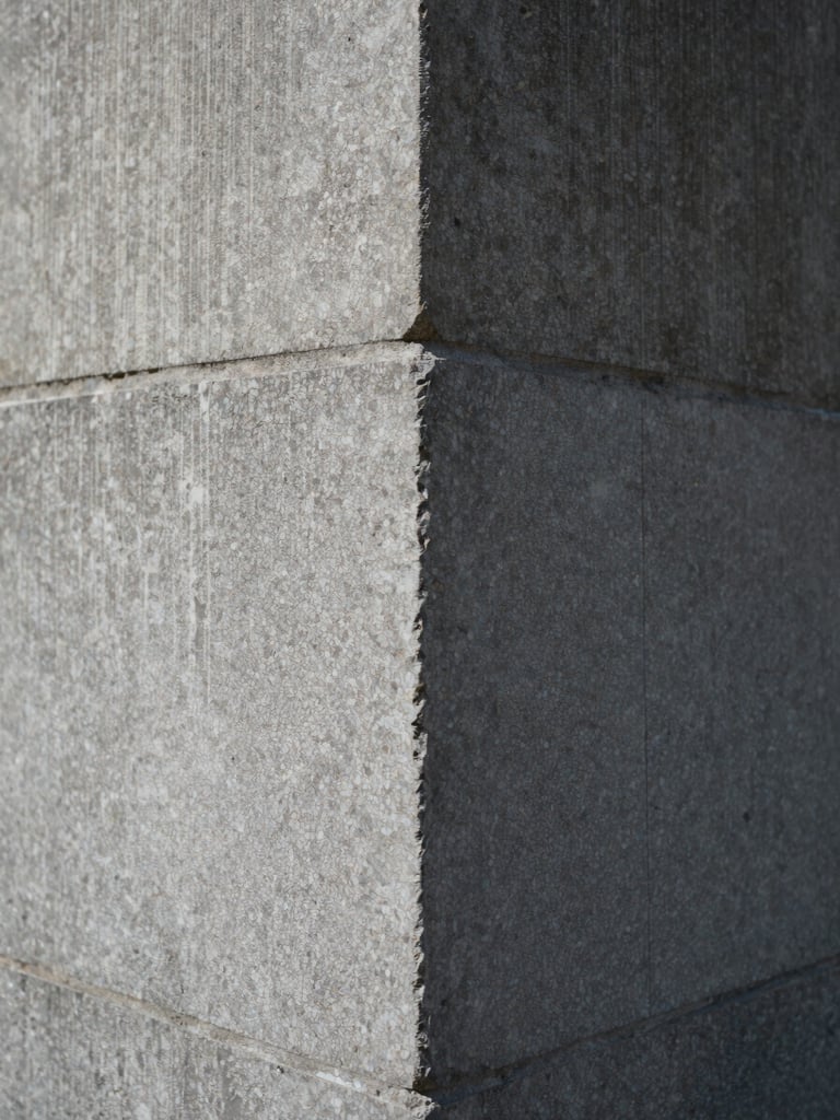 Close detail of a material transition — polished stone meeting raw concrete at a wall junction, diffused daylight raking across the surface, no people, sharp focus on texture and edge precision