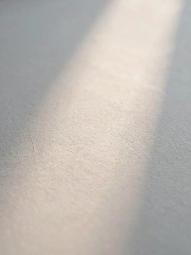 Abstract close-up of soft morning light reflecting on textured handmade paper, gentle shadows, low contrast, extremely shallow depth of field, minimalist serene composition