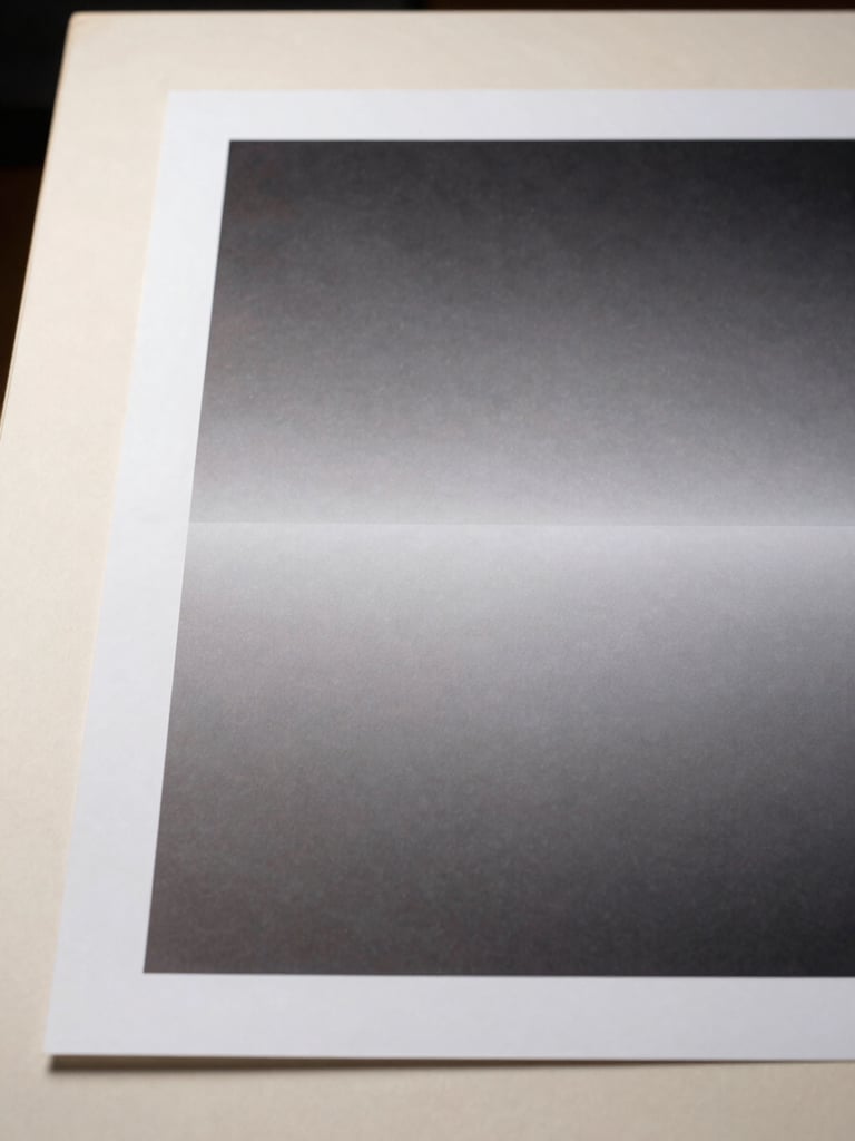 Close-up straight-on view of a finished design output — a large-format printed piece resting flat on a warm off-white surface, shot from directly above under controlled north-facing studio light, clean edges dominating the frame with a narrow strip of the surface visible at left
