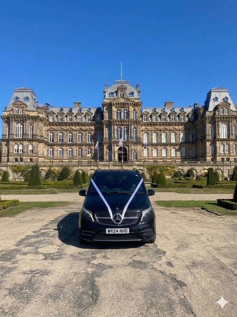 Black Mercedes wedding car with white ribbons parked in front of a grand historic manor house estate.
