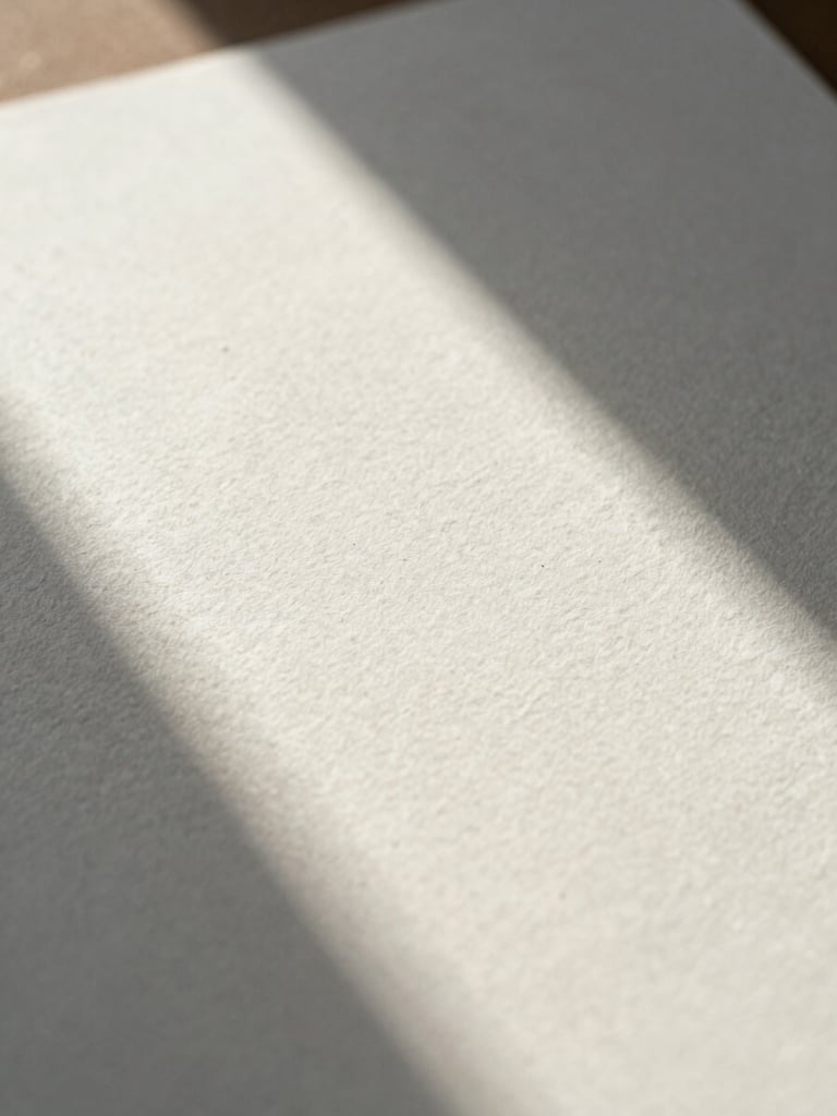 Extreme close-up of premium textured watercolor paper with soft morning shadows casting a clean geometric line across the surface.