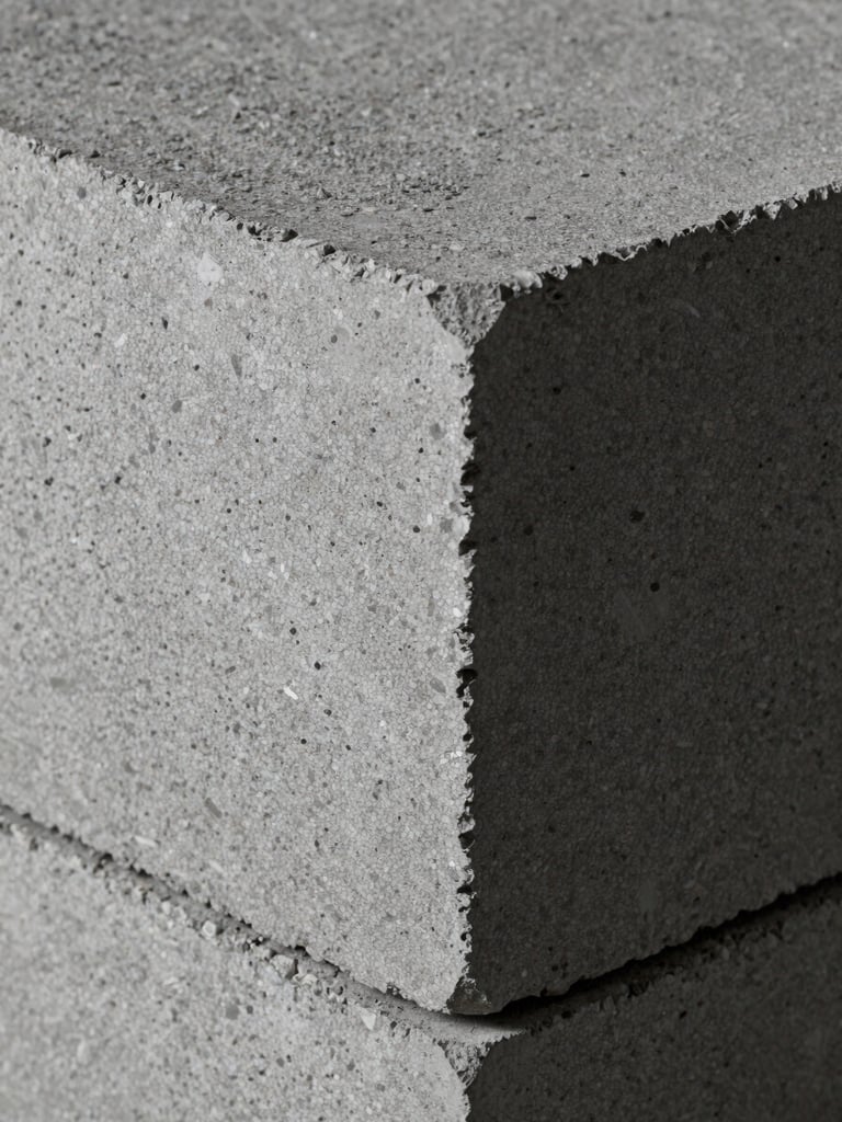 Extreme close-up of concrete block surface texture under cool studio strobe light, sharp angular edges of a standard CMU in the foreground, rough aggregate visible in the face, overhead framing, industrial grey tones