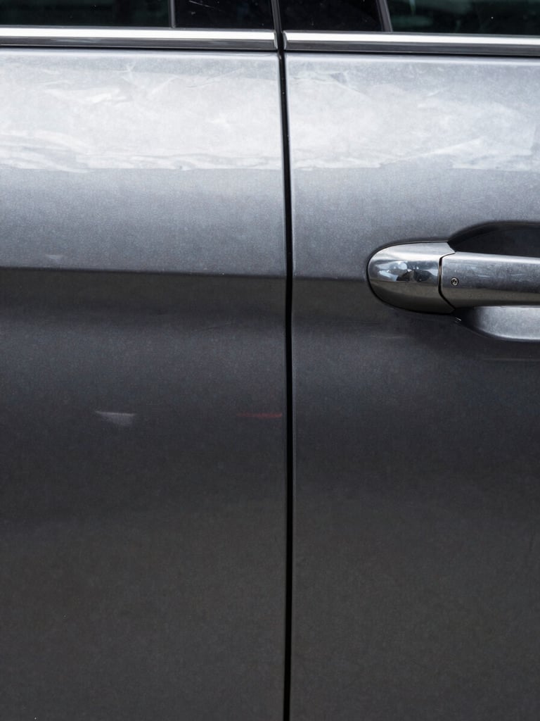 Extreme close-up of a car door panel, left half showing a sharp dent crease in dark metallic paint, right half showing the same surface perfectly restored — photographed straight-on under bright diffused studio strobes, no shadows, clinical documentation framing