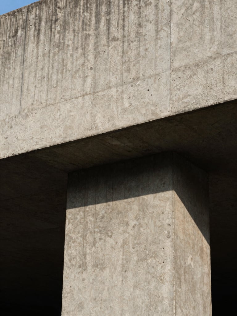 High-contrast close-up portrait of raw, textured concrete structure in Accra, hard direct midday sunlight casting deep architectural shadows, brutalist form.