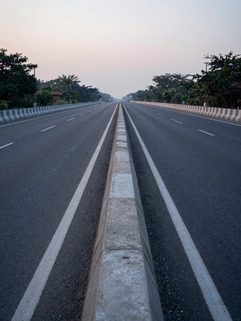 Ground-level view along the Dwarka Expressway service road at dawn, clean concrete median visible, receding perspective lines pulling the eye into a calm vanishing point, diffused cool morning light, no vehicles, empty road surface showing material texture
