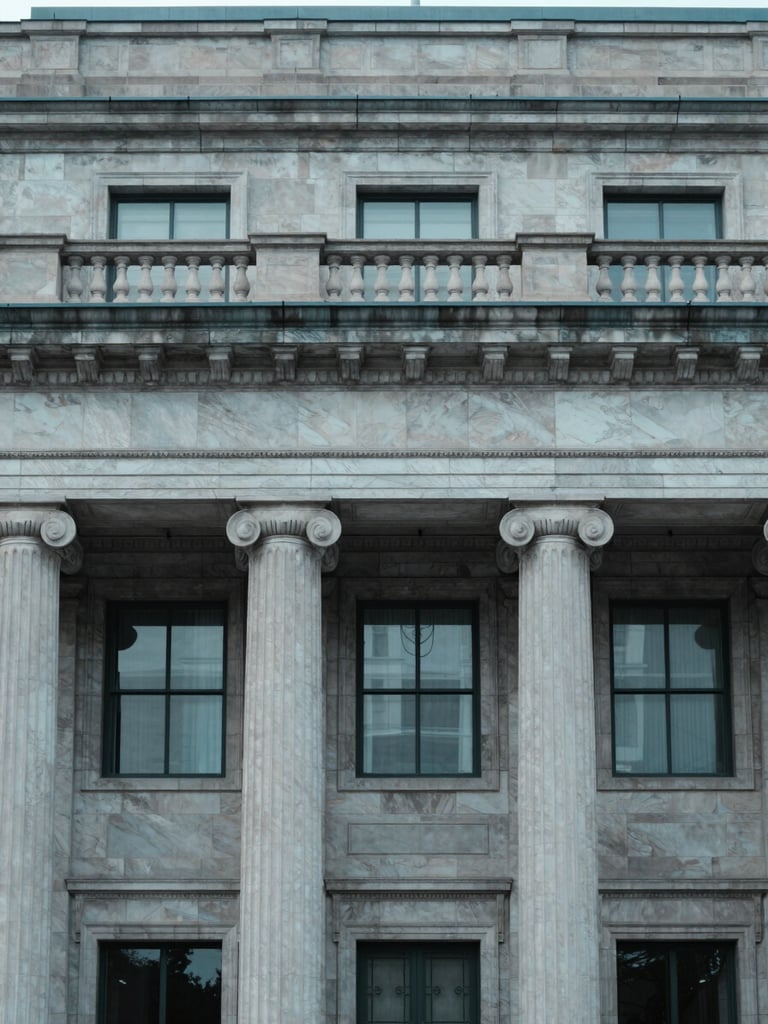 Architectural detail of a classic state treasury building facade, cool neutral daylight, desaturated corporate blue tones, 35mm