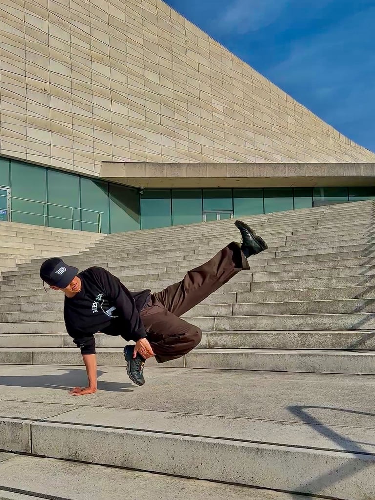 YoYo performing a breakdance move in front of concrete building.