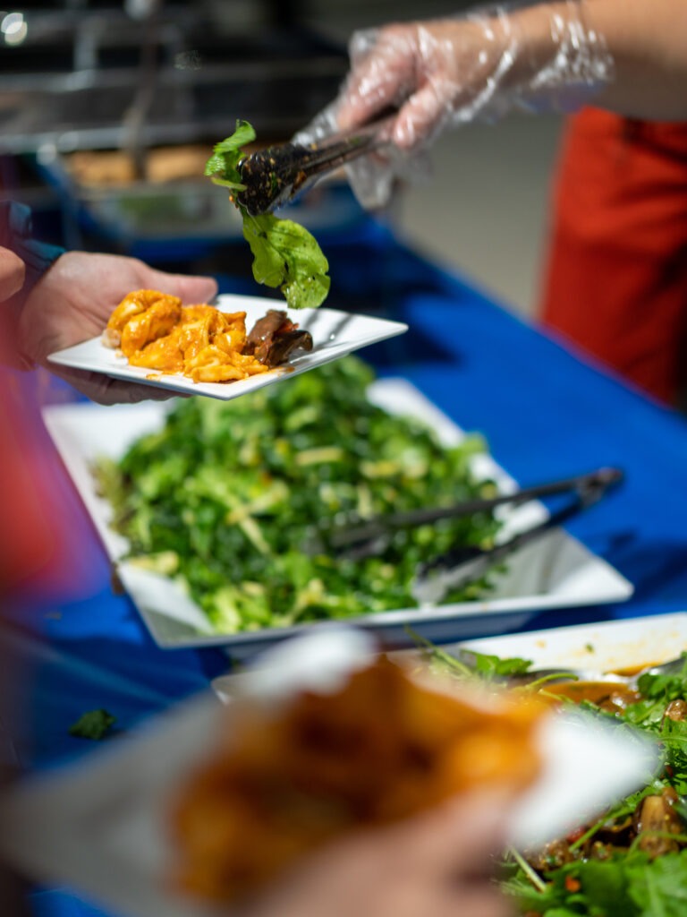 Hand serving salad with tongs onto a plate someone else is holding