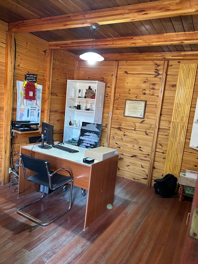 Despacho rústico en oficina con escritorio de madera y ordenador, con paredes revestidas en madera.