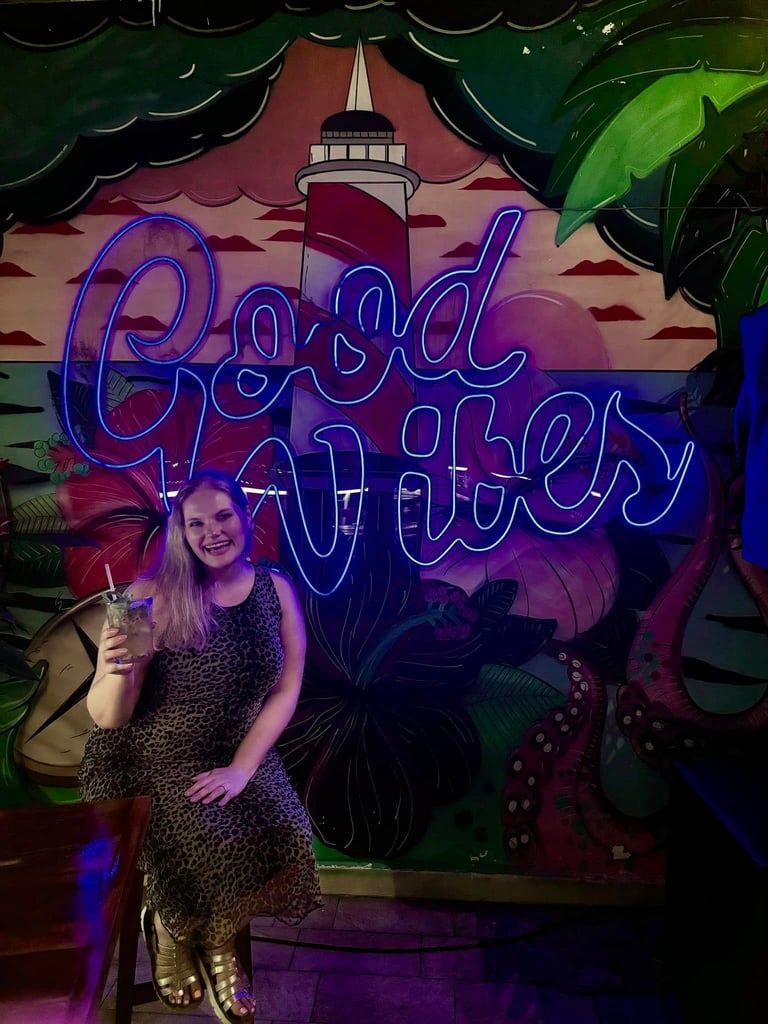 Woman holding a drink in front of neon sign saying "Good Vibes"