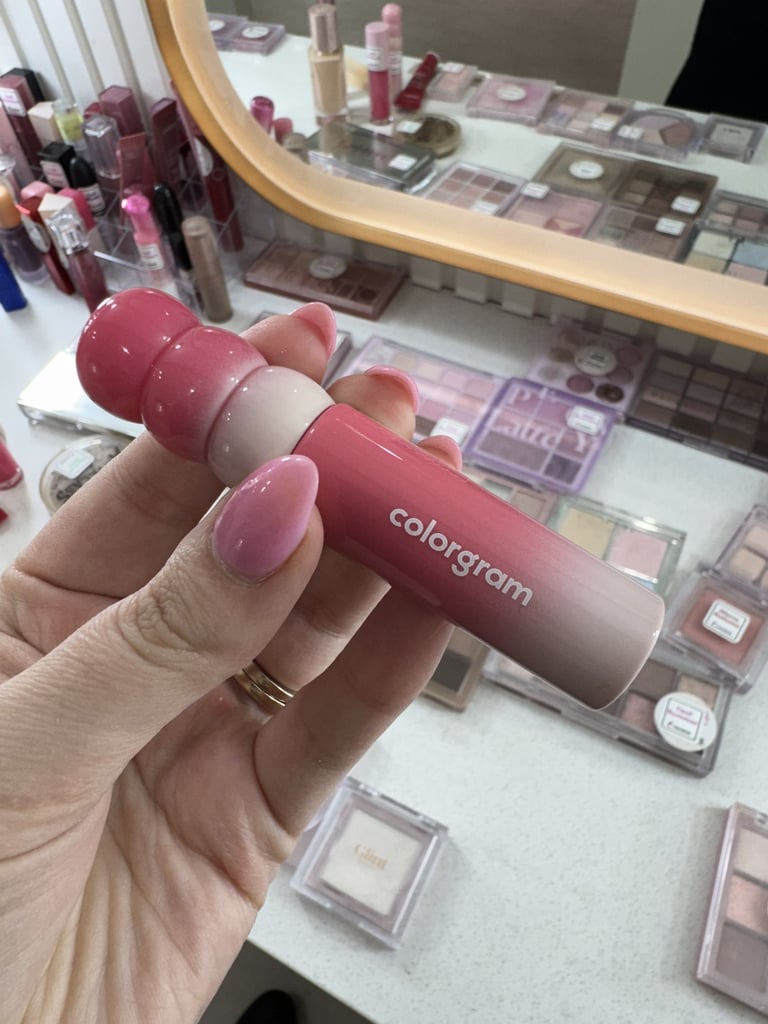 Hand holding a Colorgram pink gradient lip tint in a vanity filled with Korean beauty makeup palettes.