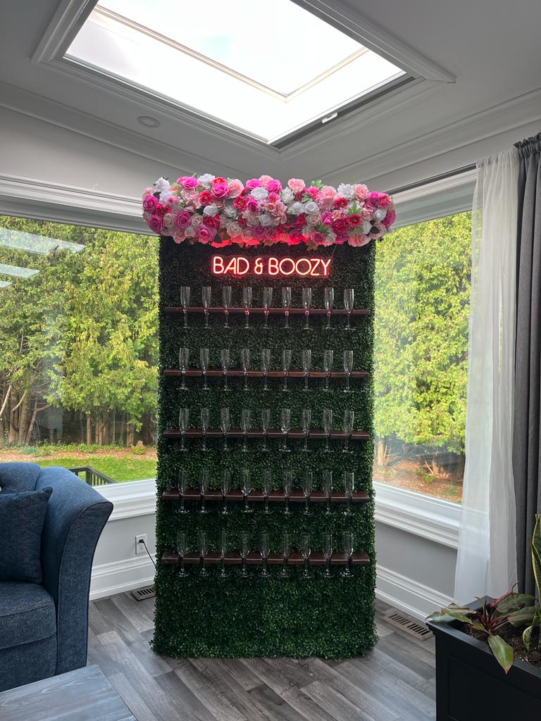 Champagne wall of assorted pink roses and a sign that says bad & Boozy