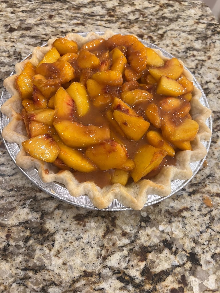 Fresh homemade peach pie with a fluted crust sitting on a granite countertop.