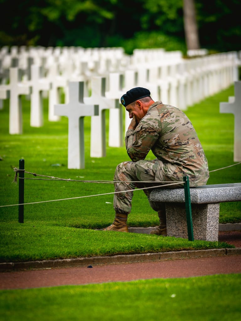 Soldat en uniforme de camouflage assis sur un banc dans un cimetière militaire, exprimant tristesse devant des croix blanches