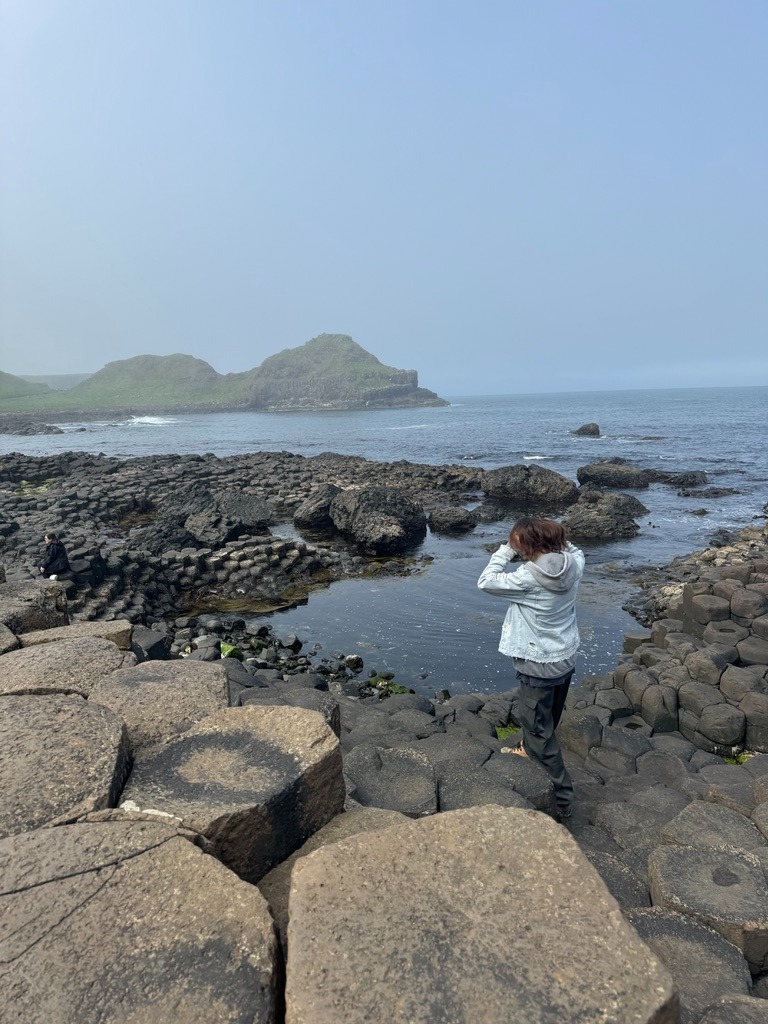 a person standing on a rock formation in the ocean, Ireland, Giant Causeway