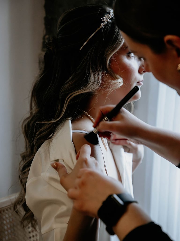 maquilleuse qui maquille les épaules d'une mariée