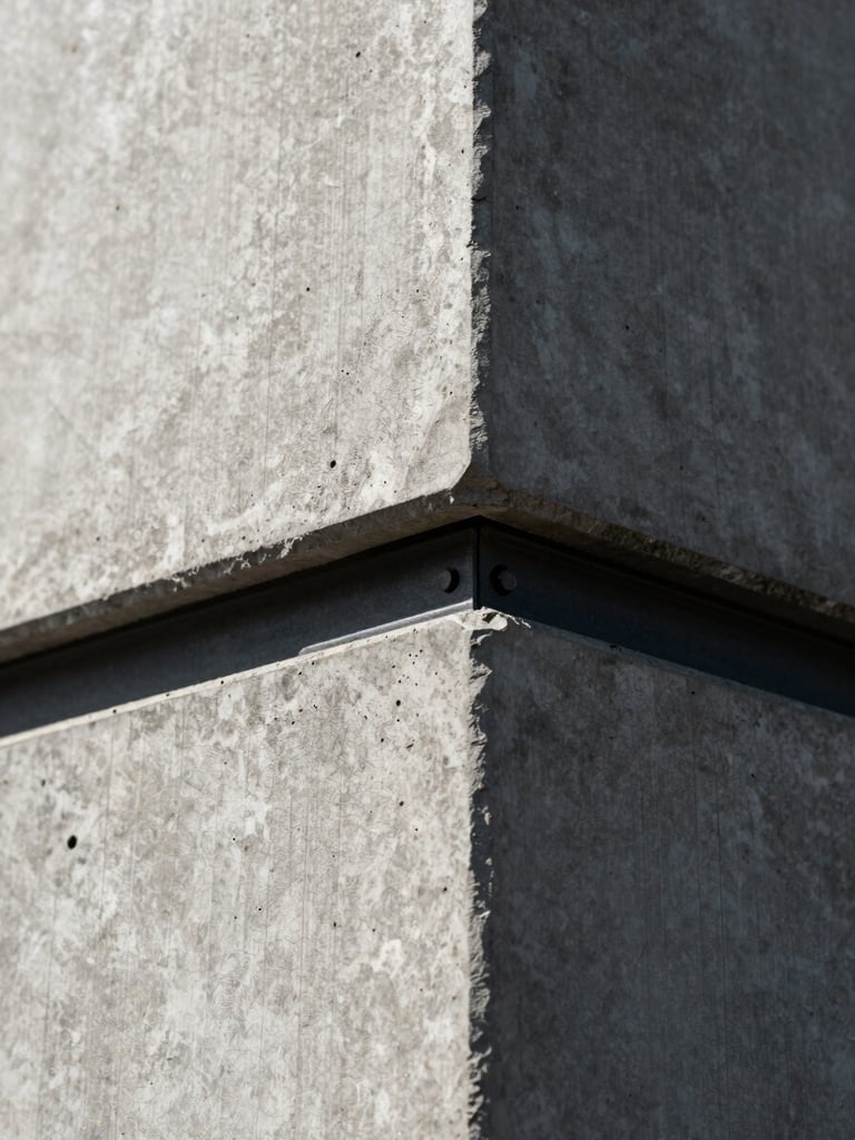 Extreme close-up architectural detail of raw concrete meeting a clean black steel joint under high-contrast directional sunlight, highlighting texture and structural precision.