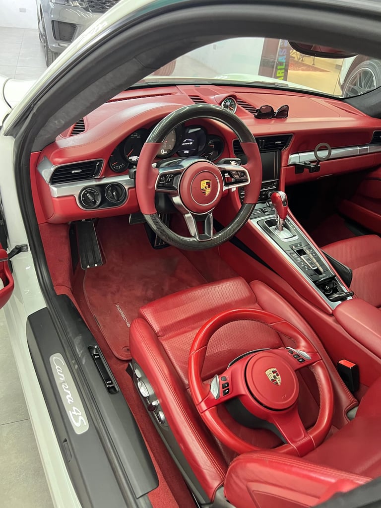 Interior view of a white Porsche Carrera 4S featuring a luxury red leather cabin and carbon fiber steering wheel.