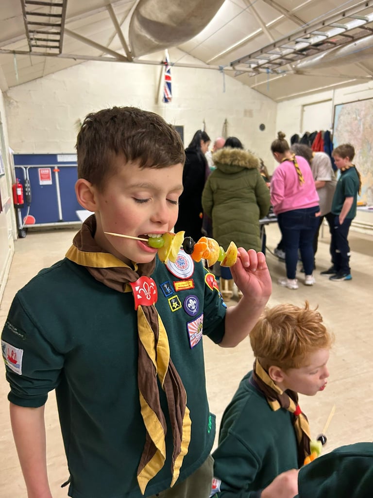 A cub from the 25th Allerton eats some fruit on a stick.