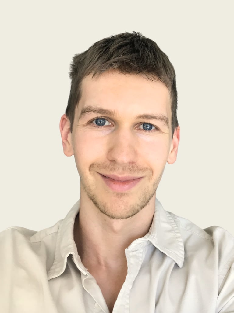 Professional headshot of a smiling young man with blue eyes and short brown hair.