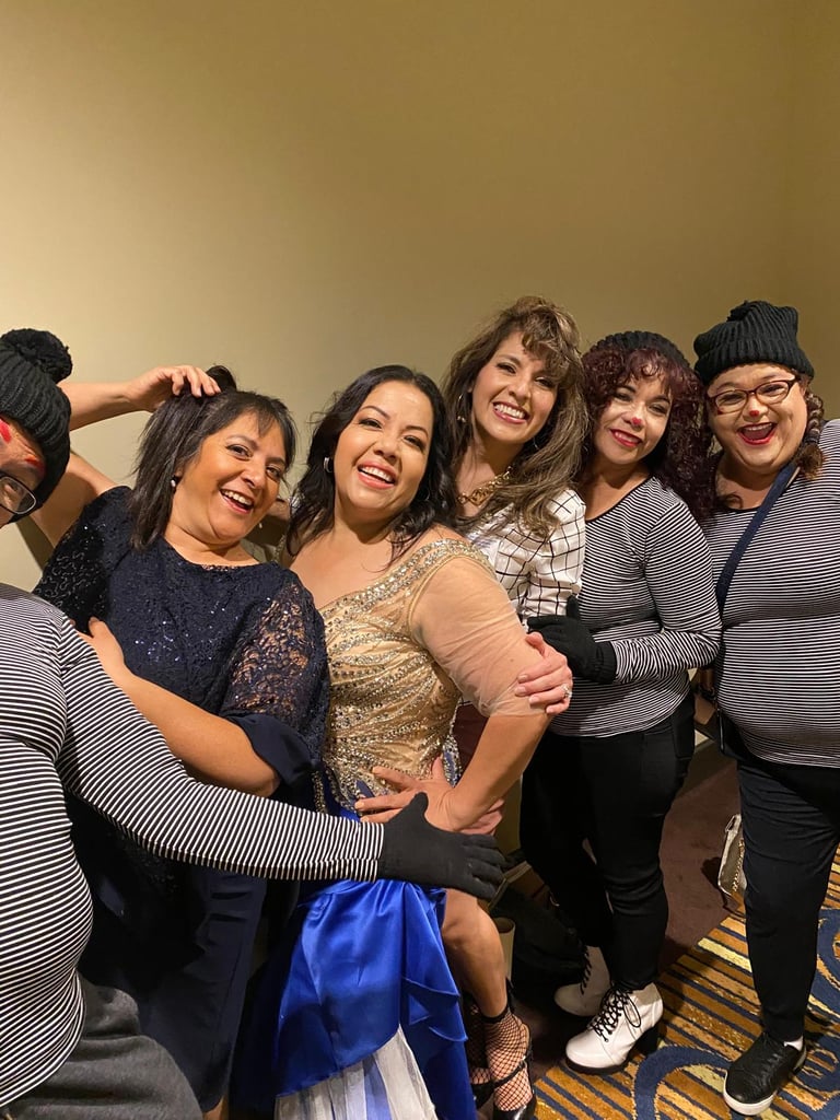 Diverse group of smiling women posing together at a party, including guests in elegant gowns and mimes in striped shirts.