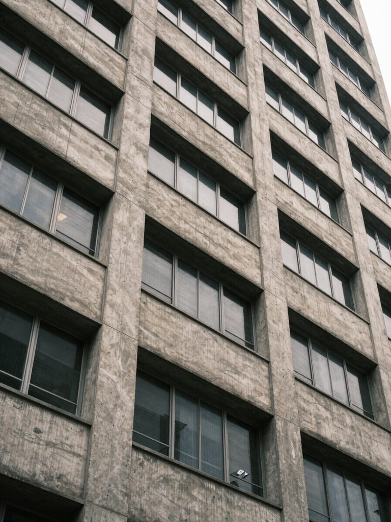 Close architectural detail of a Lagos mid-rise building facade — rendered concrete panels and aluminium window frames under even overcast daylight, shot from street level looking up at a slight angle to show structural quality and finish, no people