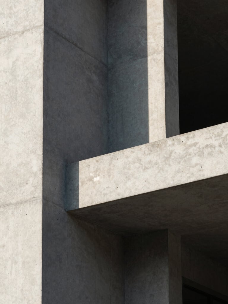 Extreme close-up of raw concrete architectural angles under harsh afternoon sunlight, casting deep geometric shadows across a clean minimalist facade.