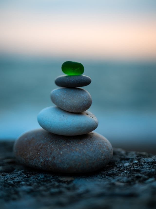 Balanced stack of smooth zen stones topped with a green sea glass piece at dusk.