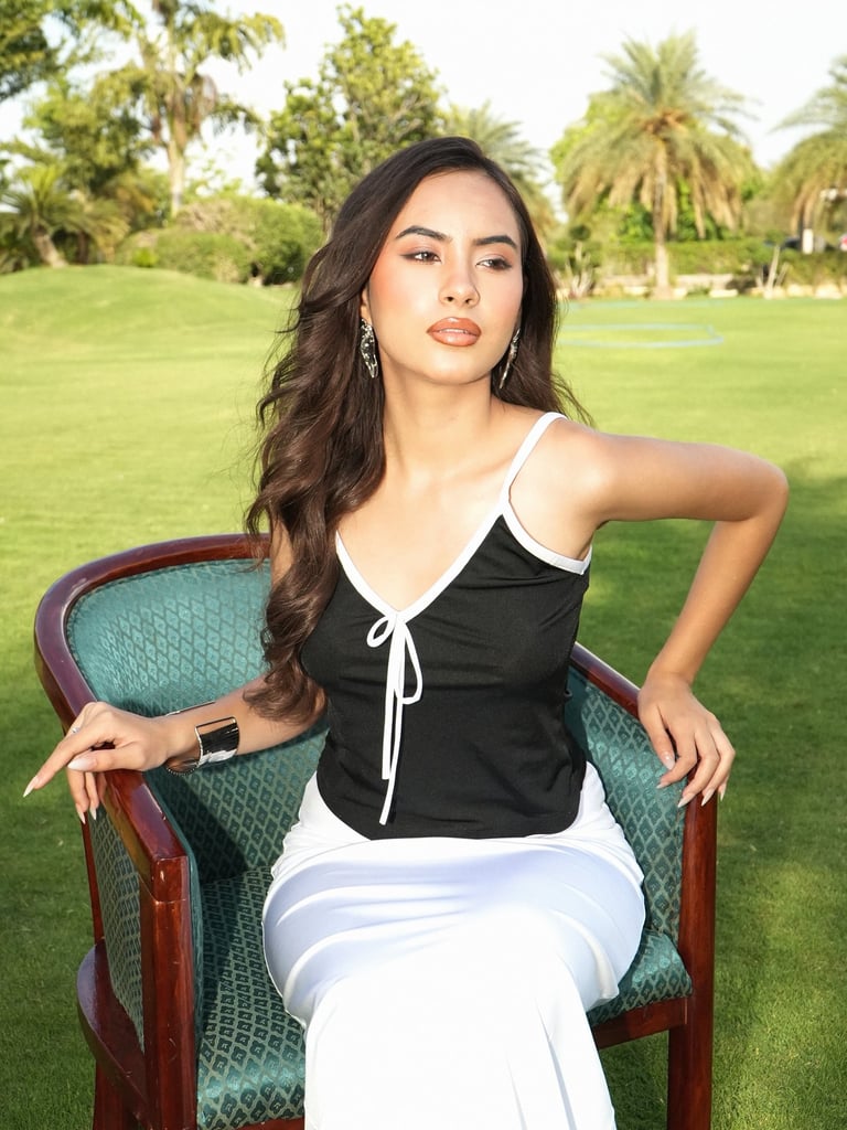 A stylish woman in a black and white top posing on a green chair in an outdoor garden setting.