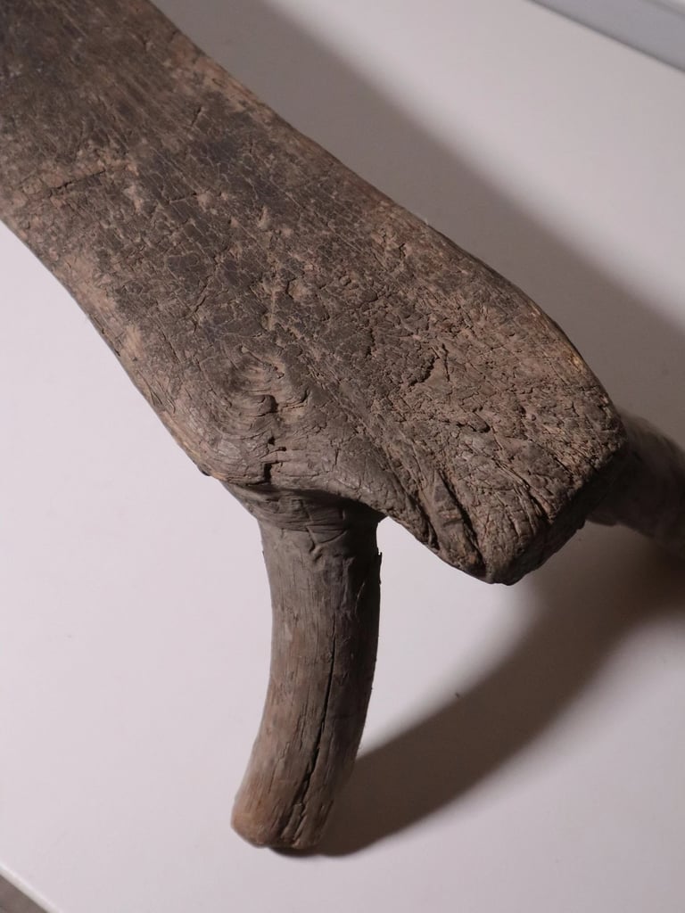 Rustic antique hand-carved wooden stool with weathered texture and organic three-legged design.