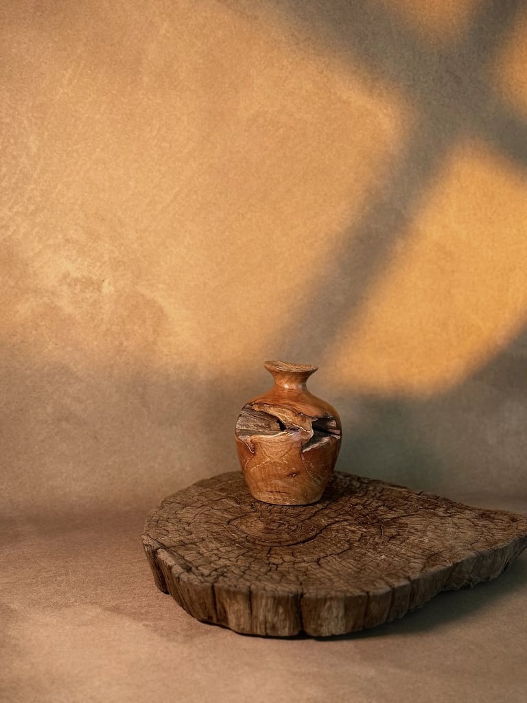 Handcrafted rustic wooden vase displayed on a live edge wood slice with warm natural lighting.