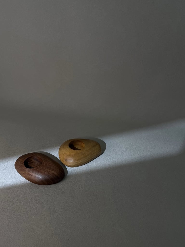 Two smooth pebble-shaped wooden tea light holders in dark walnut and light oak finishes.