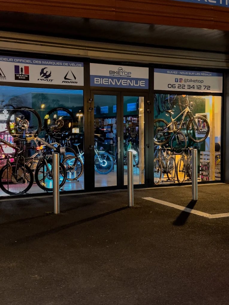 Biketop store front displaying mountain bikes and road bicycles through glass windows at night.