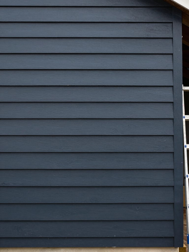 Straight-on documentary shot of a freshly painted exterior clapboard siding wall, deep charcoal paint showing even sheen, overcast daylight revealing true color without glare, ladder edge visible at one side indicating active job site