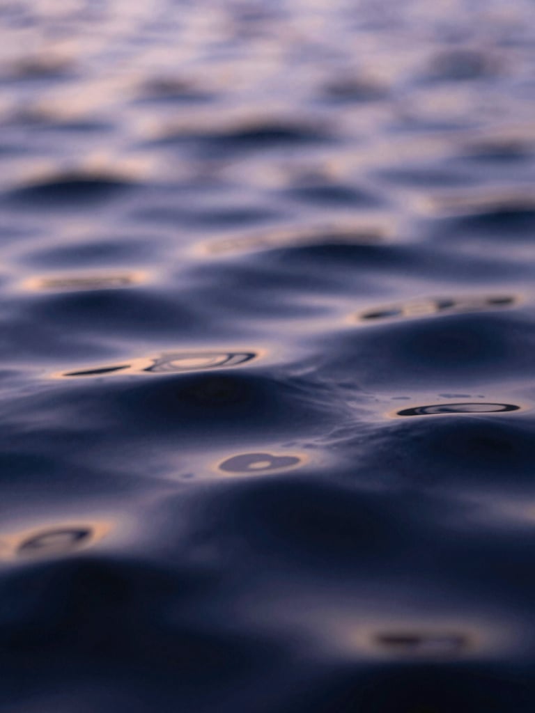 Extreme macro close-up of a textured liquid surface, dark indigo ripples reflecting pale lavender twilight, soft out-of-focus light.