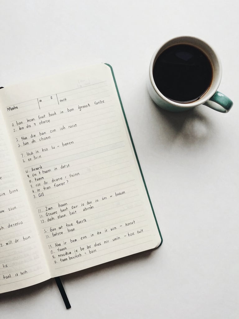 Overhead flat-lay of a clean minimalist study desk, a notebook with neat handwritten German grammar tables, a ceramic cup of coffee, soft natural overcast daylight, 35mm film aesthetic.