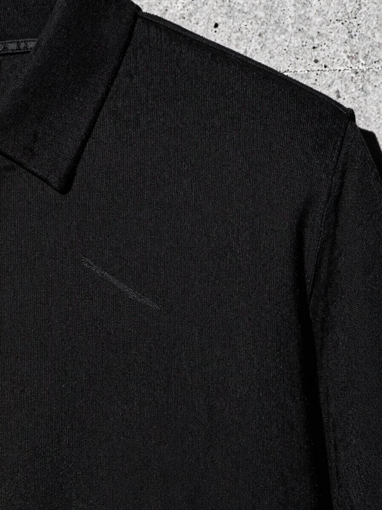 Close-up crop of heavy-weight black cotton fabric texture with clean embroidery, raw urban concrete background, high-contrast monochrome