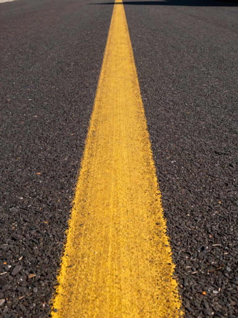 Low-angle perspective shot looking down a long, perfectly straight yellow line on dark asphalt, sharp morning light casting crisp shadows.