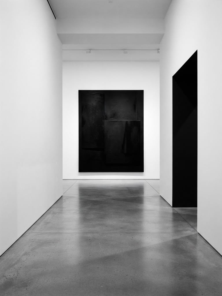 A stark, minimalist gallery interior with high-contrast shadows, clean white walls, and a large black contemporary canvas on the far wall.