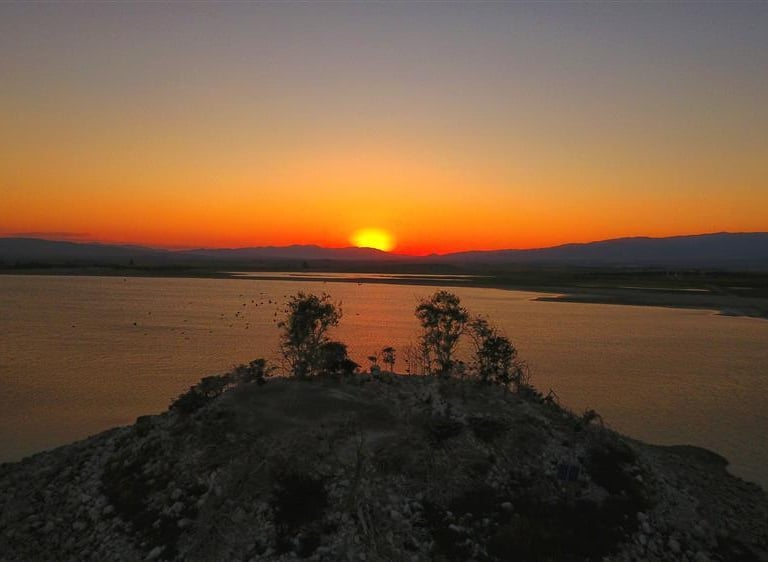 Golden sunset over a calm lake with a rocky island and silhouettes of trees against an orange sky.